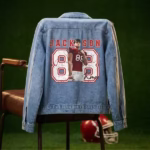 Personalized football player denim jacket displayed on a chair in a locker room setting with a team helmet.