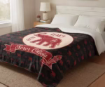 A large personalized Delta Sigma Theta blanket laid out flat across a neatly made white bed in a bright, modern bedroom, showcasing the full red and black elephant design.
